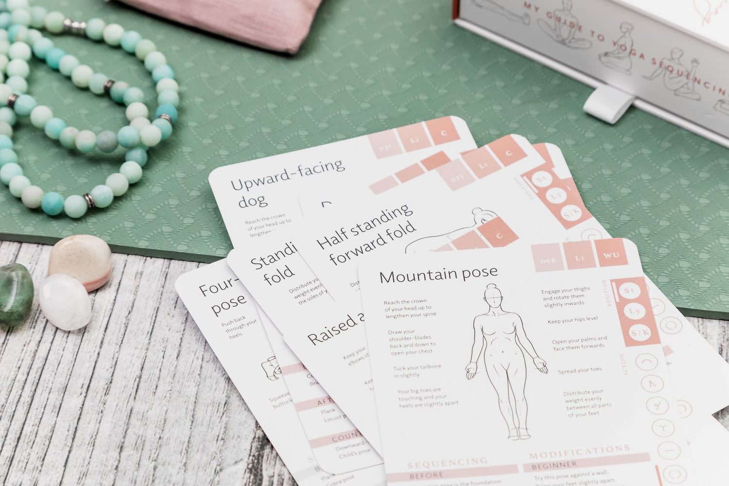 Yoga cards spread on a yoga mat showing an illustration of mountain pose on the top card with cues